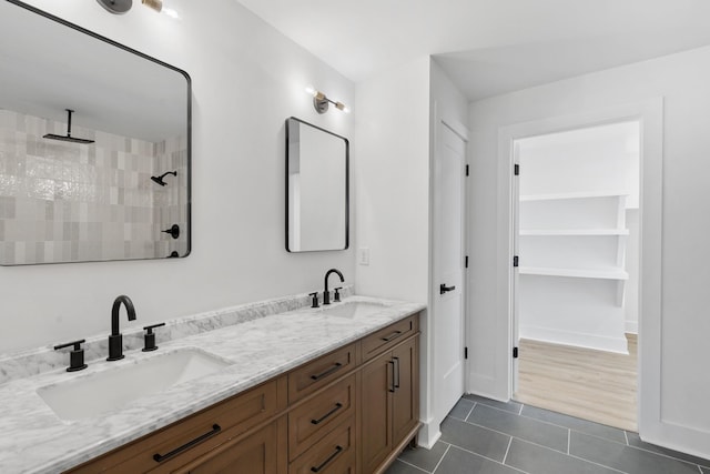 bathroom featuring tile patterned flooring, double vanity, tiled shower, and a sink