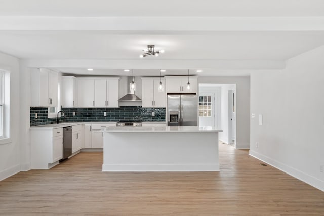 kitchen with light wood finished floors, a sink, decorative backsplash, stainless steel appliances, and wall chimney exhaust hood