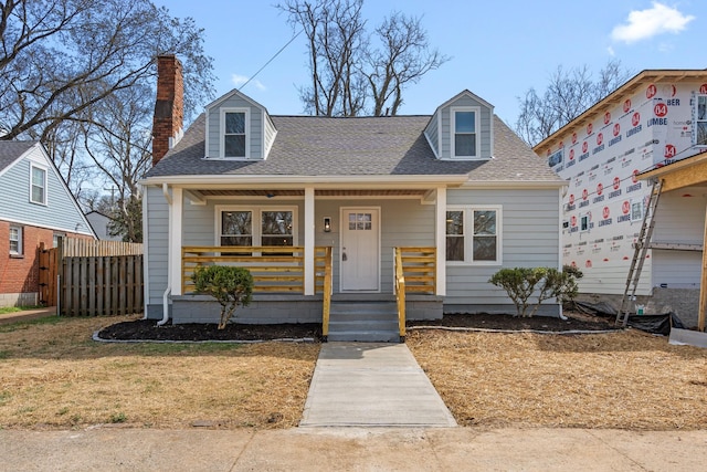 view of front of property with a front yard, roof with shingles, a porch, and a chimney