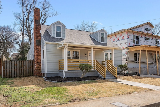 view of front of house featuring a front yard, fence, roof with shingles, a porch, and a chimney