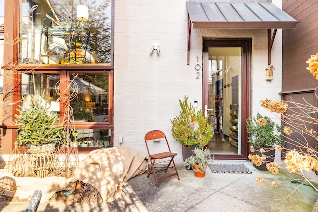 view of exterior entry featuring metal roof, a patio, brick siding, and a standing seam roof