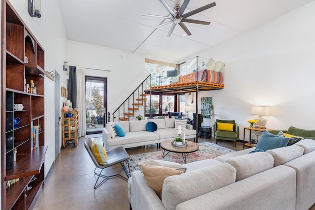 living room featuring finished concrete floors, stairs, and ceiling fan