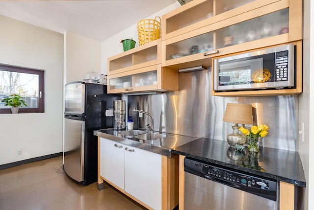 kitchen with a sink, appliances with stainless steel finishes, white cabinets, baseboards, and concrete flooring