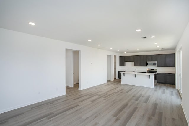 kitchen with stainless steel microwave, light wood-style floors, open floor plan, and a sink