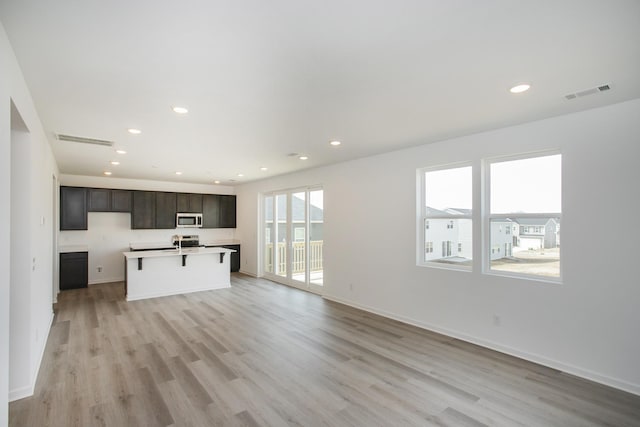 kitchen with visible vents, an island with sink, stainless steel microwave, recessed lighting, and light wood finished floors