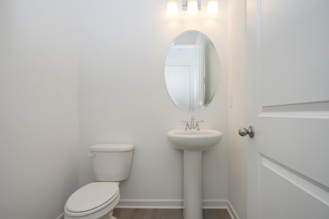 half bath featuring a sink, baseboards, toilet, and wood finished floors