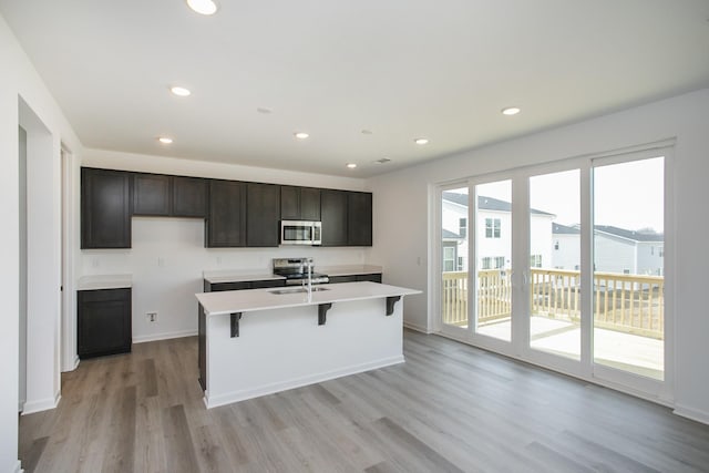 kitchen featuring recessed lighting, stainless steel microwave, light wood-style floors, and a kitchen island with sink