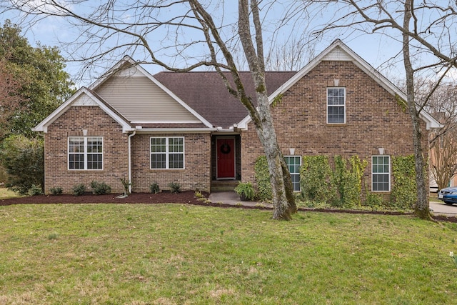 view of front facade with brick siding, a front yard, and roof with shingles