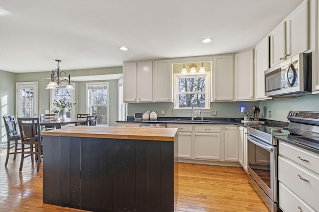 kitchen with light wood-type flooring, butcher block countertops, a sink, a kitchen island, and stainless steel appliances