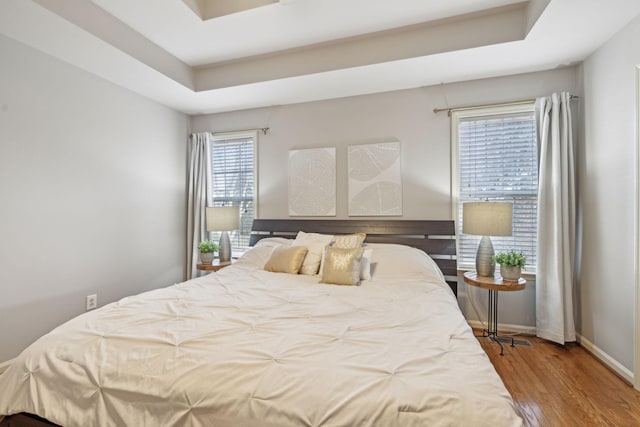 bedroom featuring baseboards, a raised ceiling, and wood finished floors