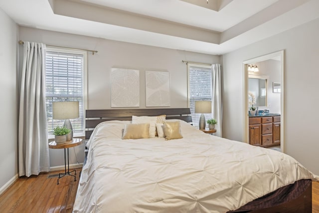 bedroom with multiple windows, a tray ceiling, and wood finished floors