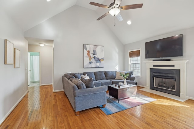 living area featuring baseboards, a fireplace with flush hearth, light wood-type flooring, high vaulted ceiling, and a ceiling fan