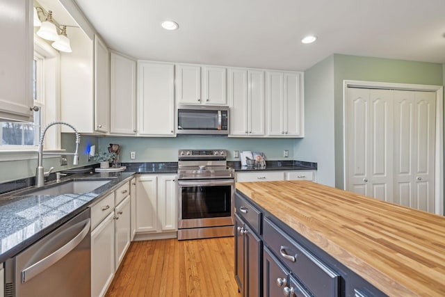 kitchen with a sink, appliances with stainless steel finishes, white cabinets, and butcher block counters