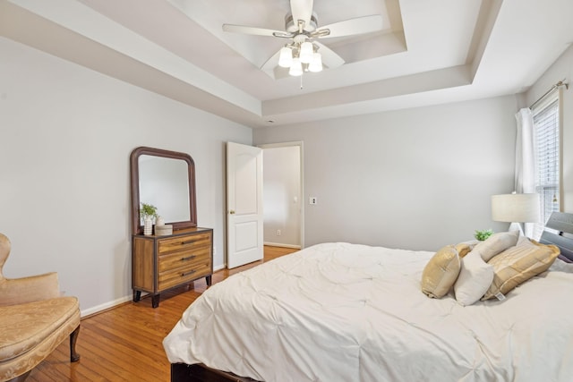 bedroom featuring ceiling fan, light wood-type flooring, a raised ceiling, and baseboards