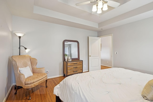 bedroom featuring a ceiling fan, a raised ceiling, baseboards, and wood-type flooring