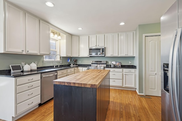 kitchen with light wood finished floors, white cabinets, stainless steel appliances, wood counters, and a sink