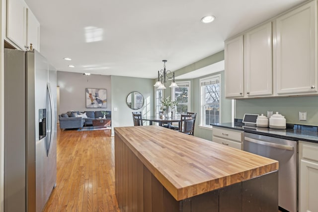 kitchen featuring light wood finished floors, decorative light fixtures, open floor plan, appliances with stainless steel finishes, and wood counters