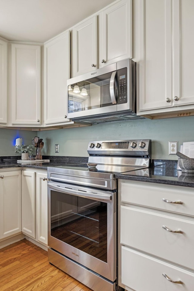 kitchen featuring white cabinets, stainless steel appliances, light wood-type flooring, and dark stone countertops