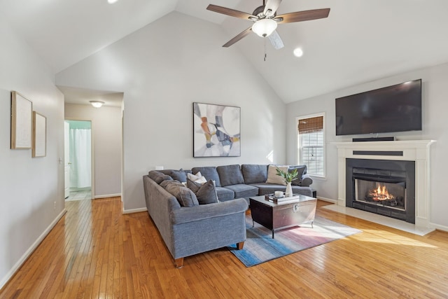 living area featuring a ceiling fan, baseboards, high vaulted ceiling, a fireplace with flush hearth, and light wood-type flooring