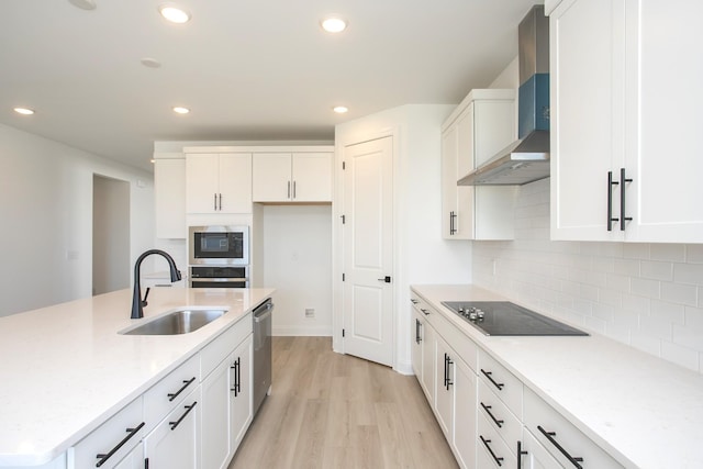 kitchen featuring light wood finished floors, stainless steel appliances, a sink, white cabinets, and wall chimney range hood