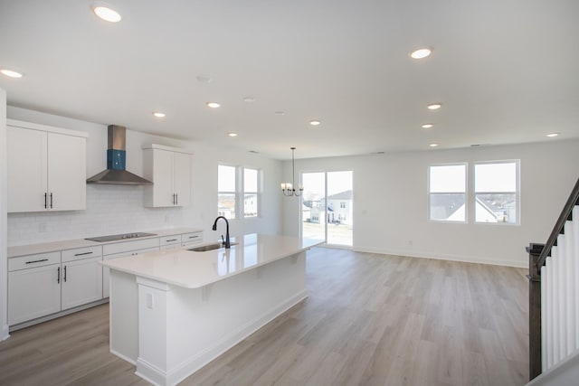 kitchen with tasteful backsplash, a center island with sink, wall chimney exhaust hood, black electric cooktop, and a sink