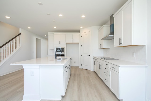 kitchen featuring light wood finished floors, a sink, wall chimney range hood, black electric cooktop, and backsplash