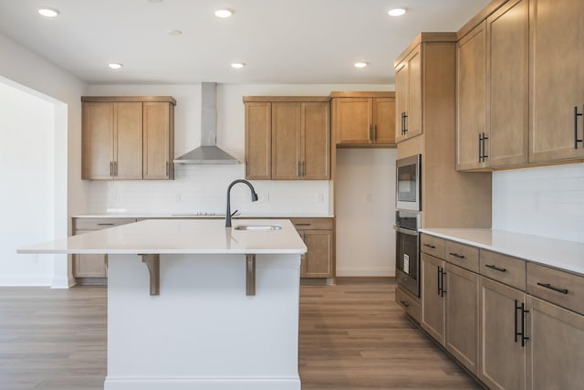 kitchen with light wood-style flooring, appliances with stainless steel finishes, wall chimney exhaust hood, and light countertops