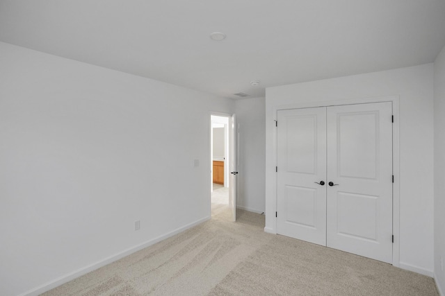 unfurnished bedroom featuring a closet, light colored carpet, and baseboards