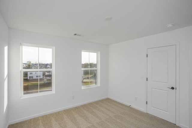 spare room featuring light colored carpet, visible vents, and baseboards