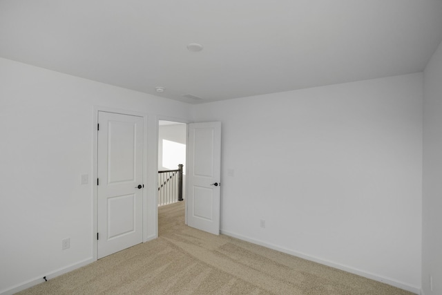 spare room featuring light colored carpet and baseboards