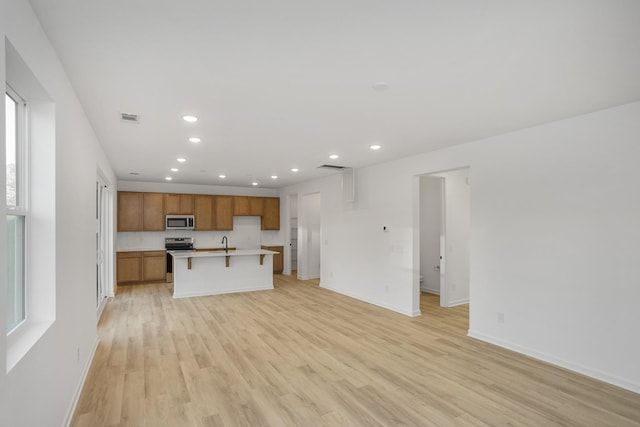 kitchen with visible vents, light wood-type flooring, stainless steel appliances, open floor plan, and brown cabinets