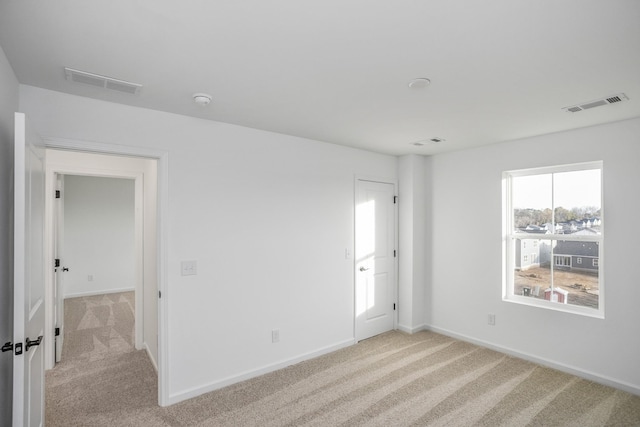 spare room with visible vents, light carpet, and baseboards