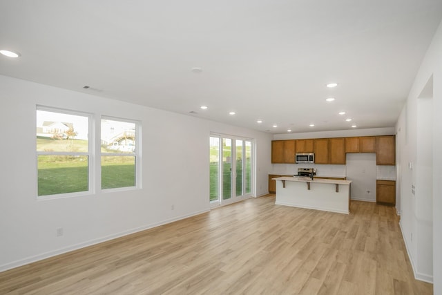 kitchen with open floor plan, recessed lighting, light wood-style flooring, brown cabinets, and stainless steel appliances