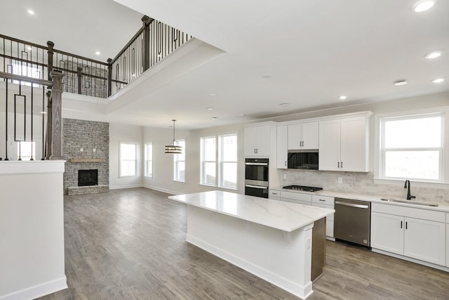 kitchen with double wall oven, a sink, gas stovetop, a stone fireplace, and dishwasher