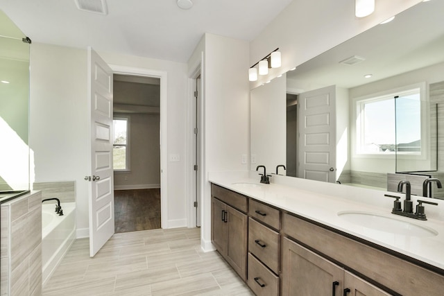 bathroom with double vanity, a bath, visible vents, and a sink