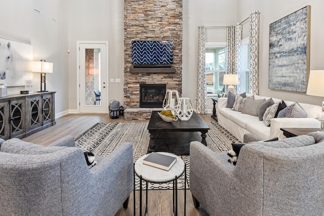 living room featuring baseboards, a high ceiling, wood finished floors, and a fireplace