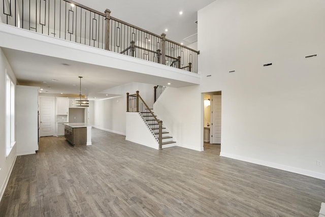 unfurnished living room with recessed lighting, baseboards, wood finished floors, and stairs