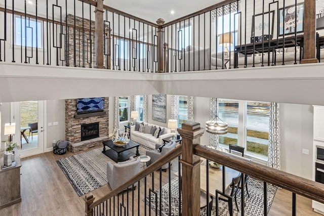 living area featuring a stone fireplace, a healthy amount of sunlight, a towering ceiling, and wood finished floors