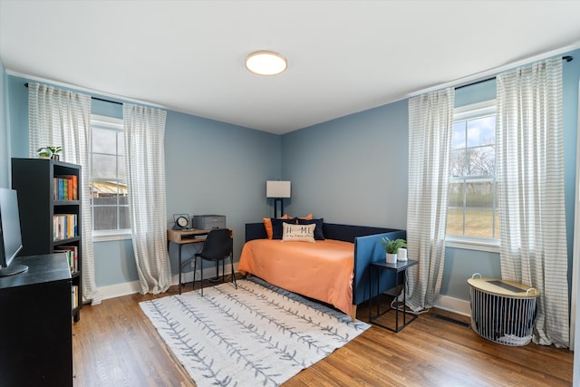 bedroom with multiple windows, baseboards, and wood finished floors