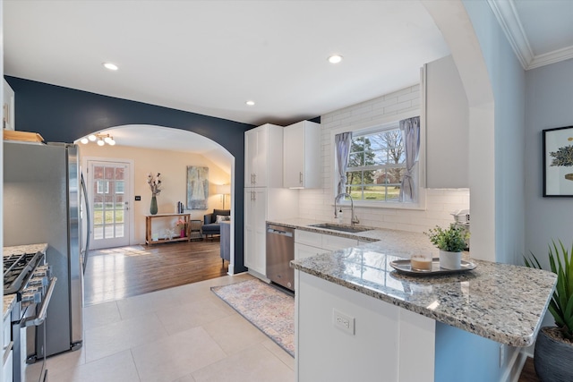 kitchen featuring light tile patterned floors, appliances with stainless steel finishes, arched walkways, white cabinetry, and a sink