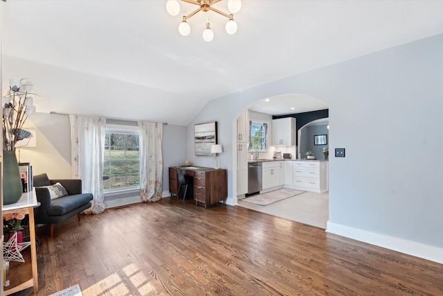 unfurnished living room with vaulted ceiling, light wood-style flooring, arched walkways, and a wealth of natural light