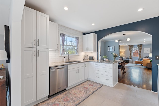 kitchen with arched walkways, dishwasher, light tile patterned flooring, and a sink