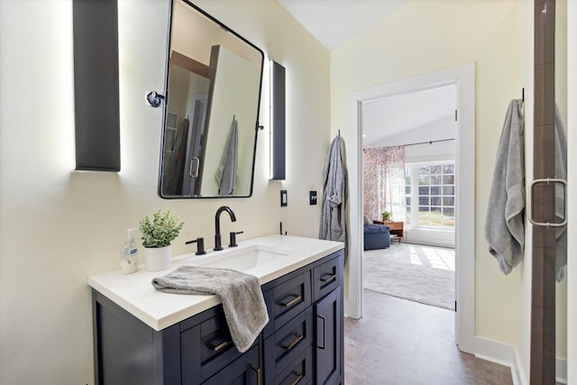 bathroom with baseboards, vanity, and lofted ceiling