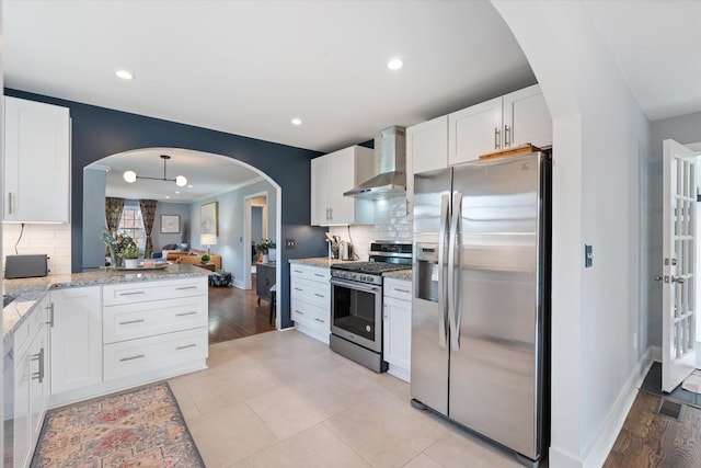 kitchen featuring white cabinets, appliances with stainless steel finishes, wall chimney exhaust hood, and light stone countertops