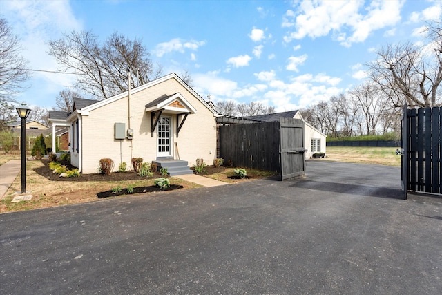 bungalow-style house featuring aphalt driveway, a gate, fence, and brick siding