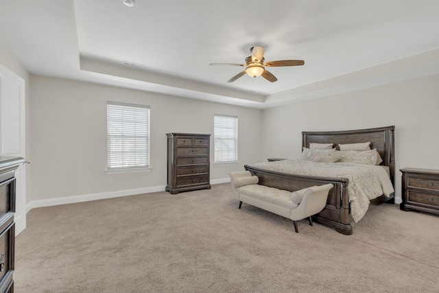 carpeted bedroom featuring a tray ceiling, visible vents, baseboards, and ceiling fan