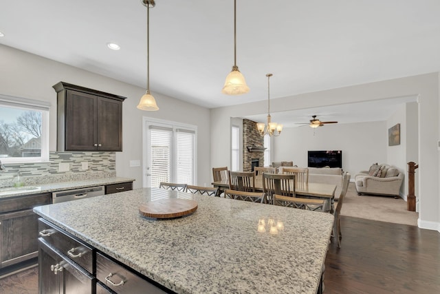 kitchen with backsplash, dark brown cabinetry, light stone counters, stainless steel dishwasher, and a sink