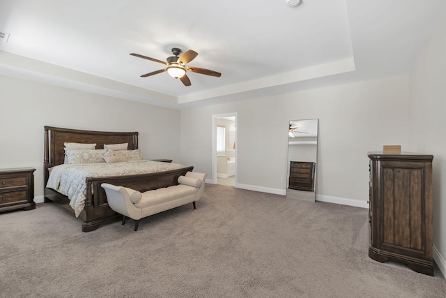 bedroom with ceiling fan, baseboards, carpet, a tray ceiling, and ensuite bath