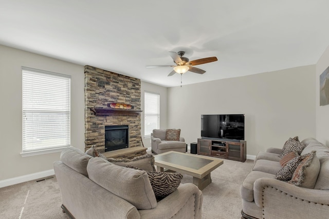 living room featuring baseboards, light carpet, a stone fireplace, and a ceiling fan