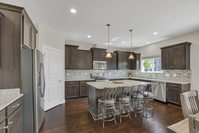 kitchen featuring a kitchen island, dark brown cabinetry, appliances with stainless steel finishes, and dark wood-type flooring